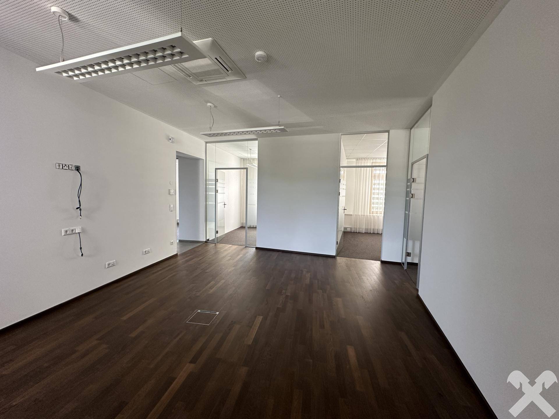 Großzügiger Bürobereich mit Holzboden und mehreren Glasabtrennungen, die separate Arbeitsräume schaffen.