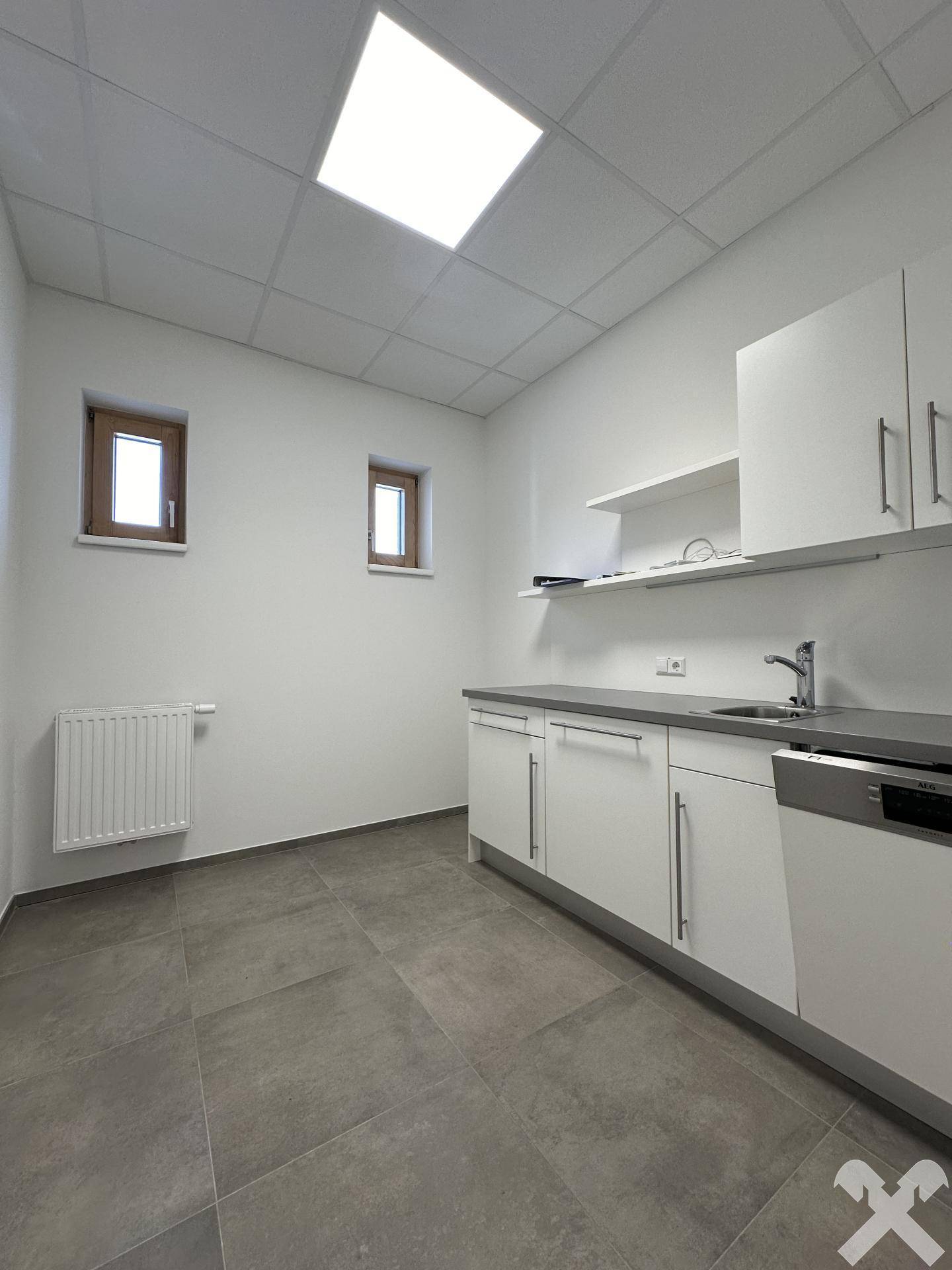 Funktionale Teeküche mit weißen Schränken, Spülmaschine und Fliesenboden, ideal für Mitarbeiterpausen.