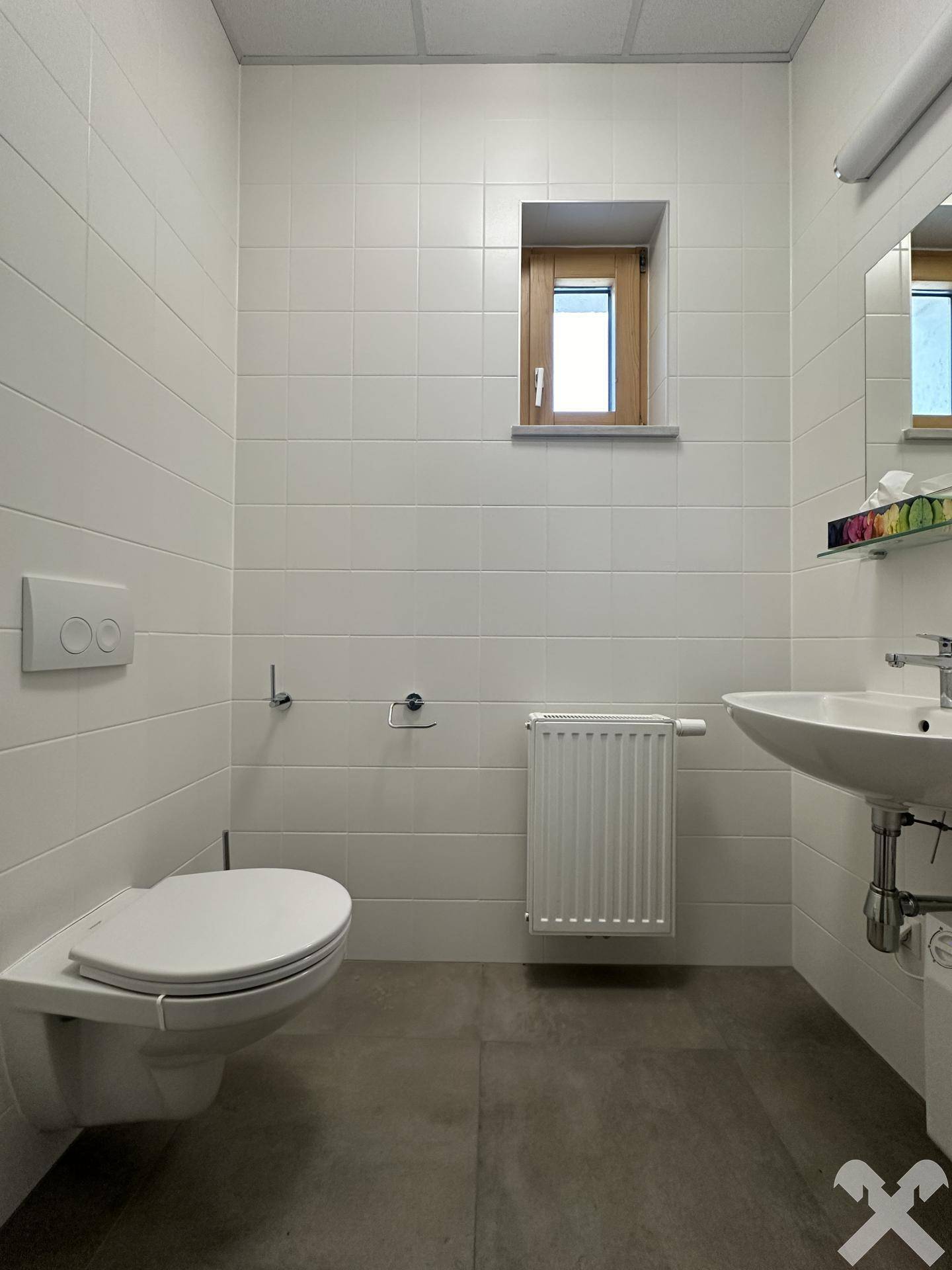 Modernes WC mit wandhängender Toilette, Waschbecken und kleinem Fenster, hell gefliest und gut gepflegt.