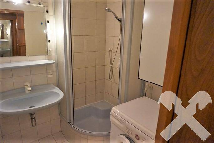 Kleines Badezimmer mit Dusche, Waschbecken und Waschmaschine, hell gefliest und funktional.