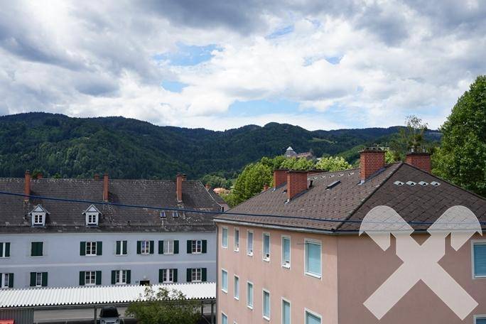 Weitläufiger Blick über Dächer und grüne Hügel, mit bewölktem Himmel und Fernsicht.