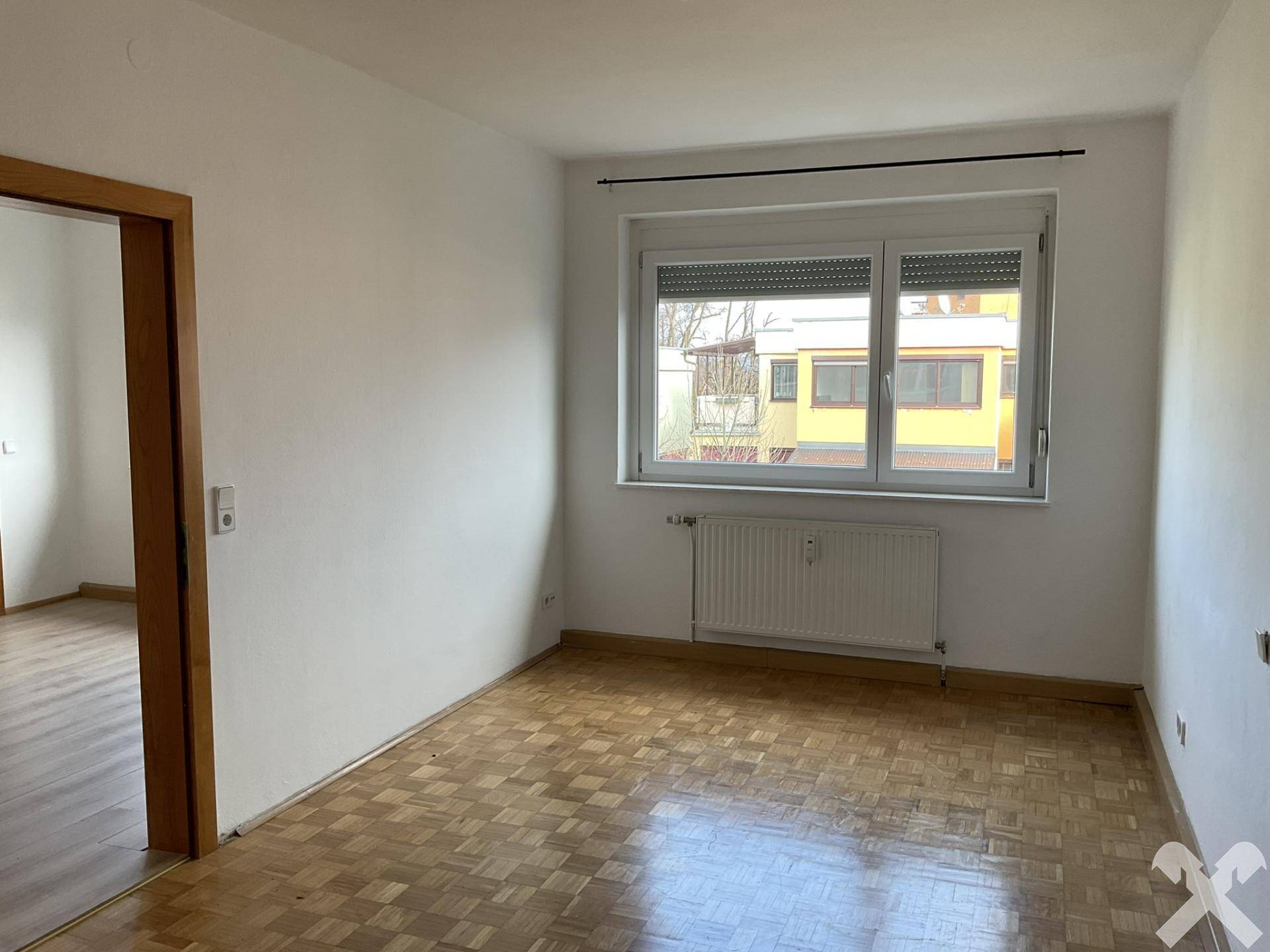 Helles Zimmer mit Parkettboden und Fenster mit Rollladen, geeignet als Schlaf- oder Arbeitszimmer.