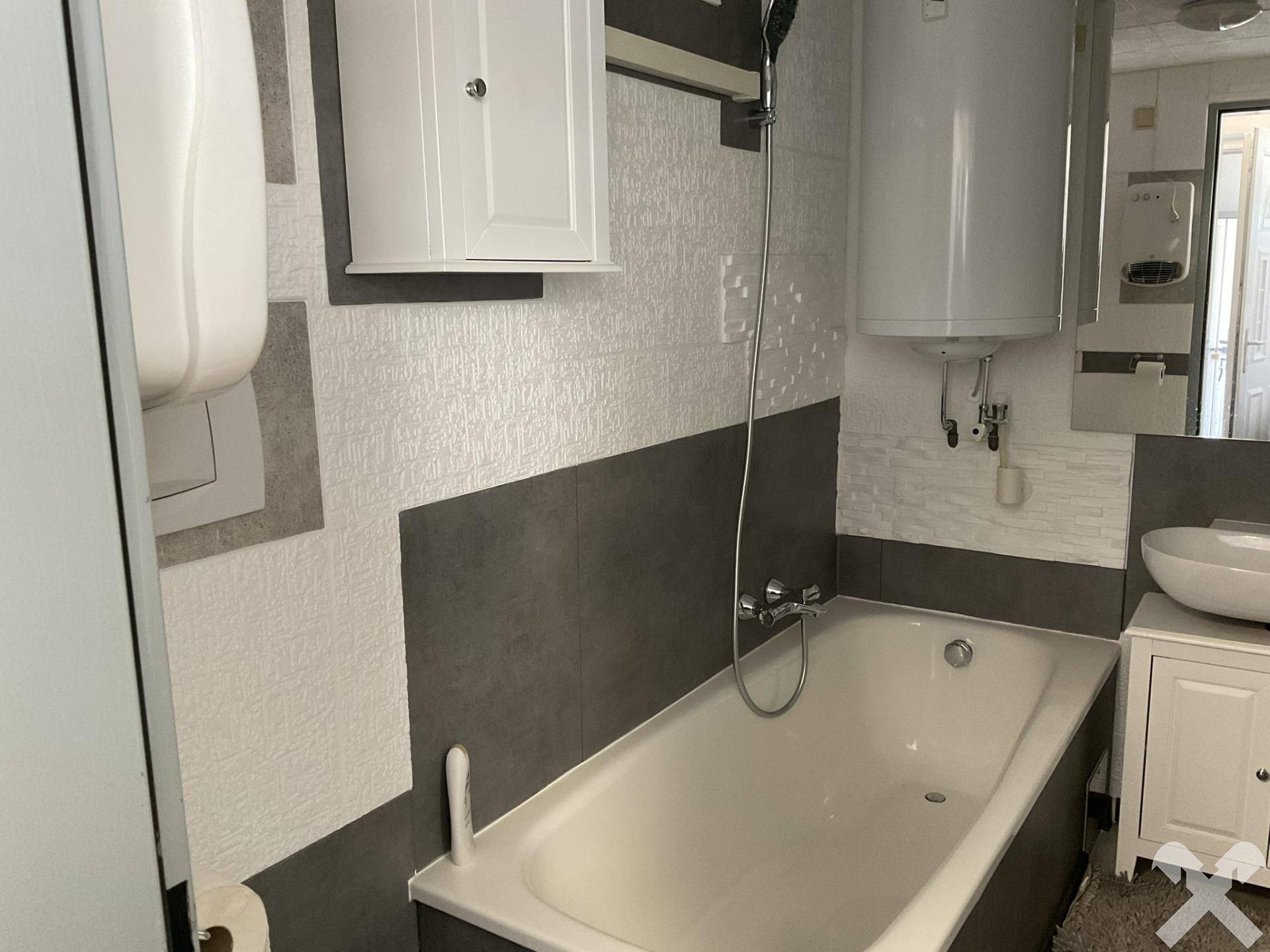 Badezimmer mit Badewanne, Waschbecken und modernen Fliesen in Grau und Weiß.