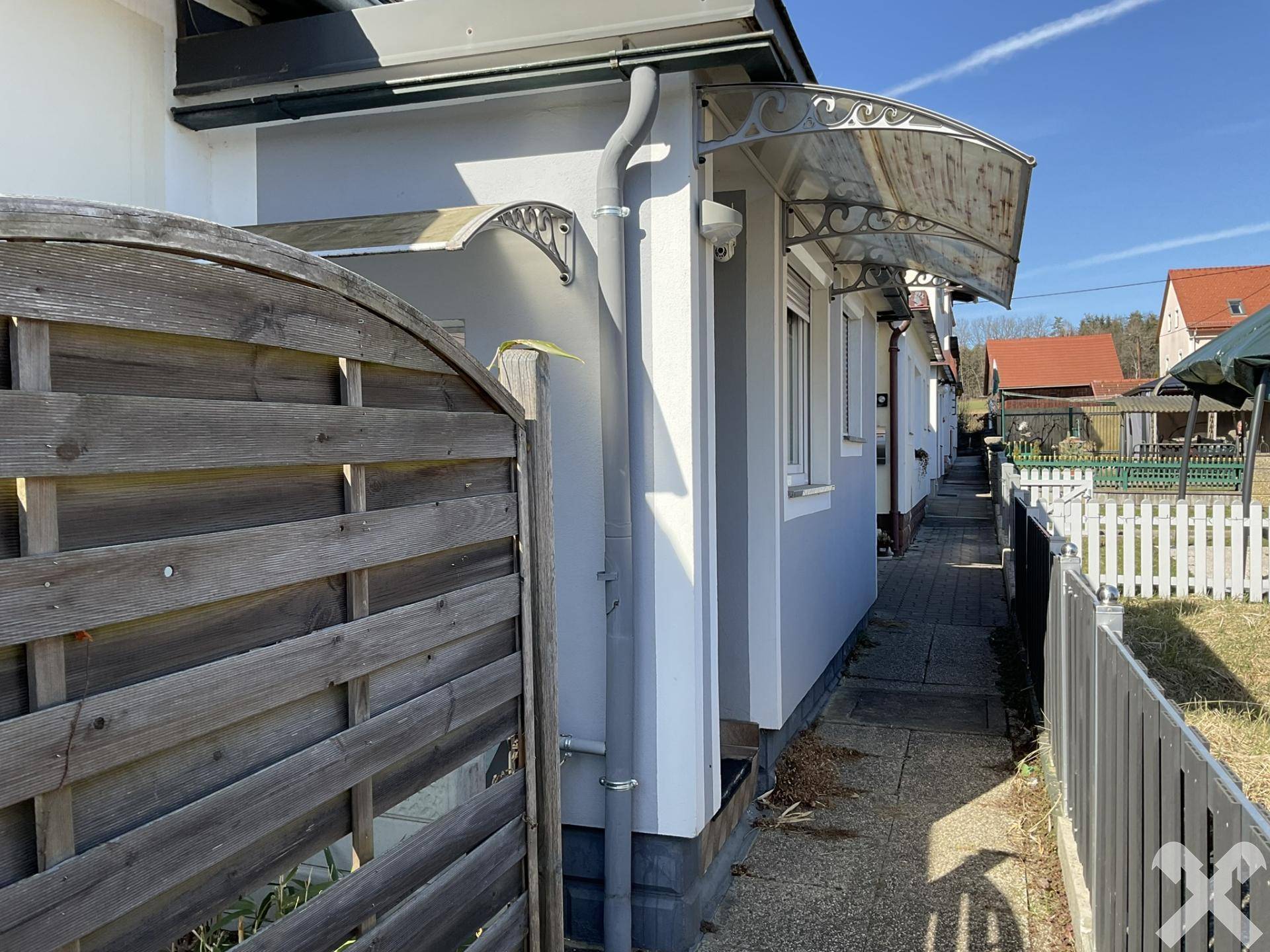 Seitenansicht des Hauses mit schmalem Zugangsweg und Holzzaun.