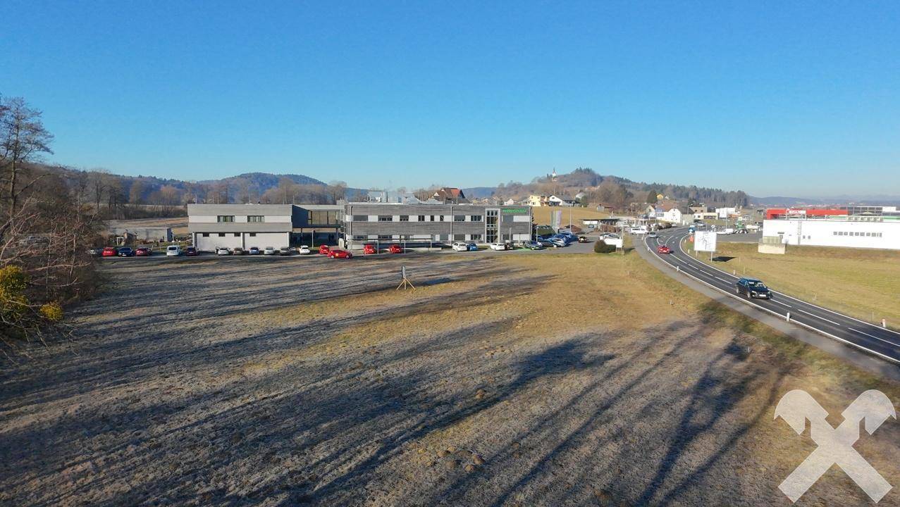Panoramablick auf ein großes Grundstück an einer Landstraße mit angrenzenden Gewerbebauten und hügeliger Landschaft.