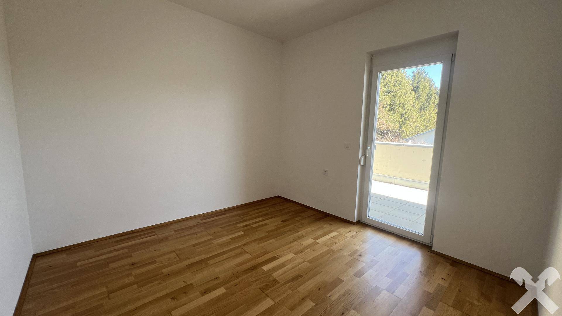 Helles Zimmer mit Holzboden und Zugang zu einem Balkon oder einer Terrasse.