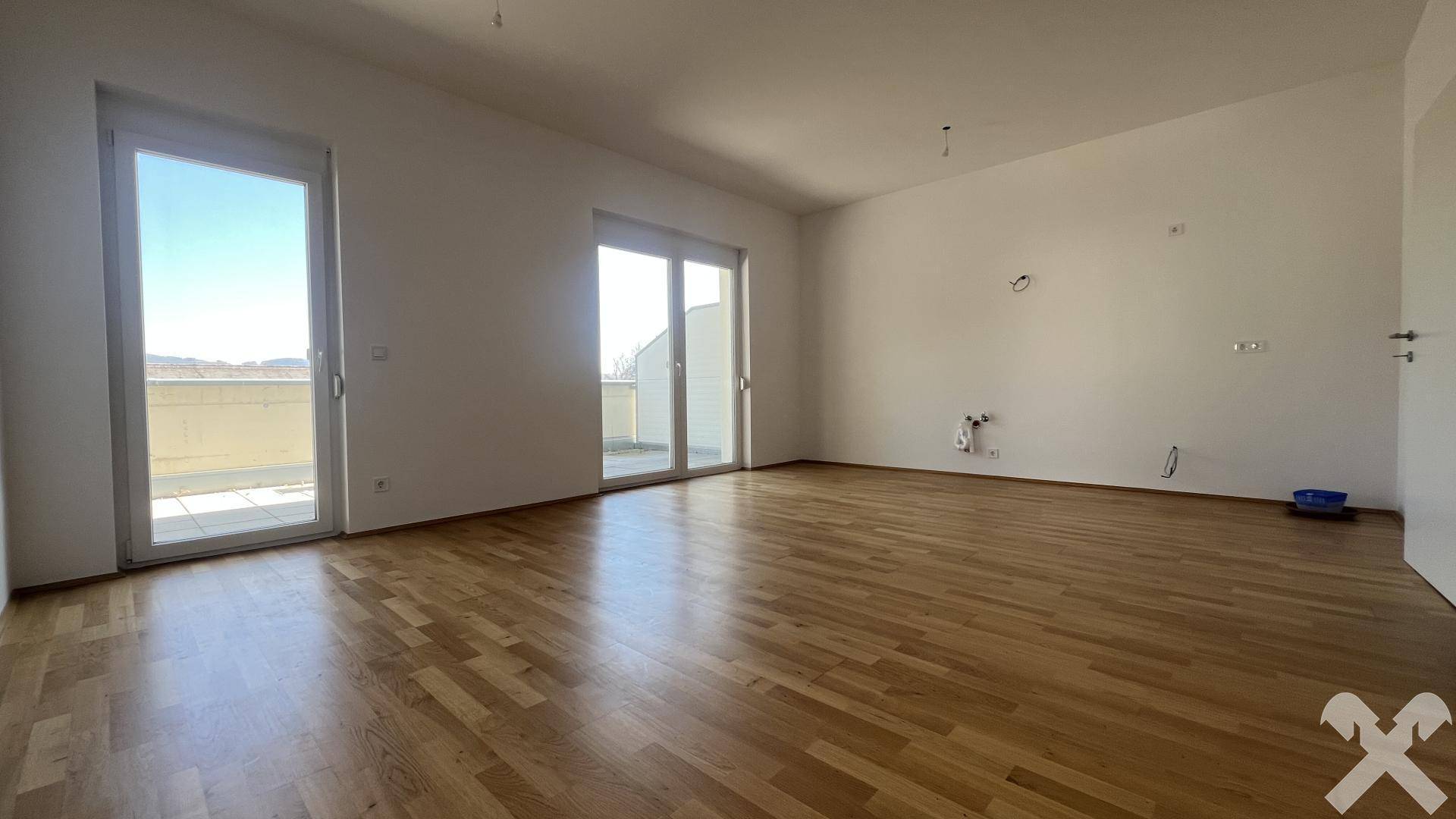 Geräumiger, heller Wohnbereich mit Holzboden und zwei Zugängen zur Außenterrasse.