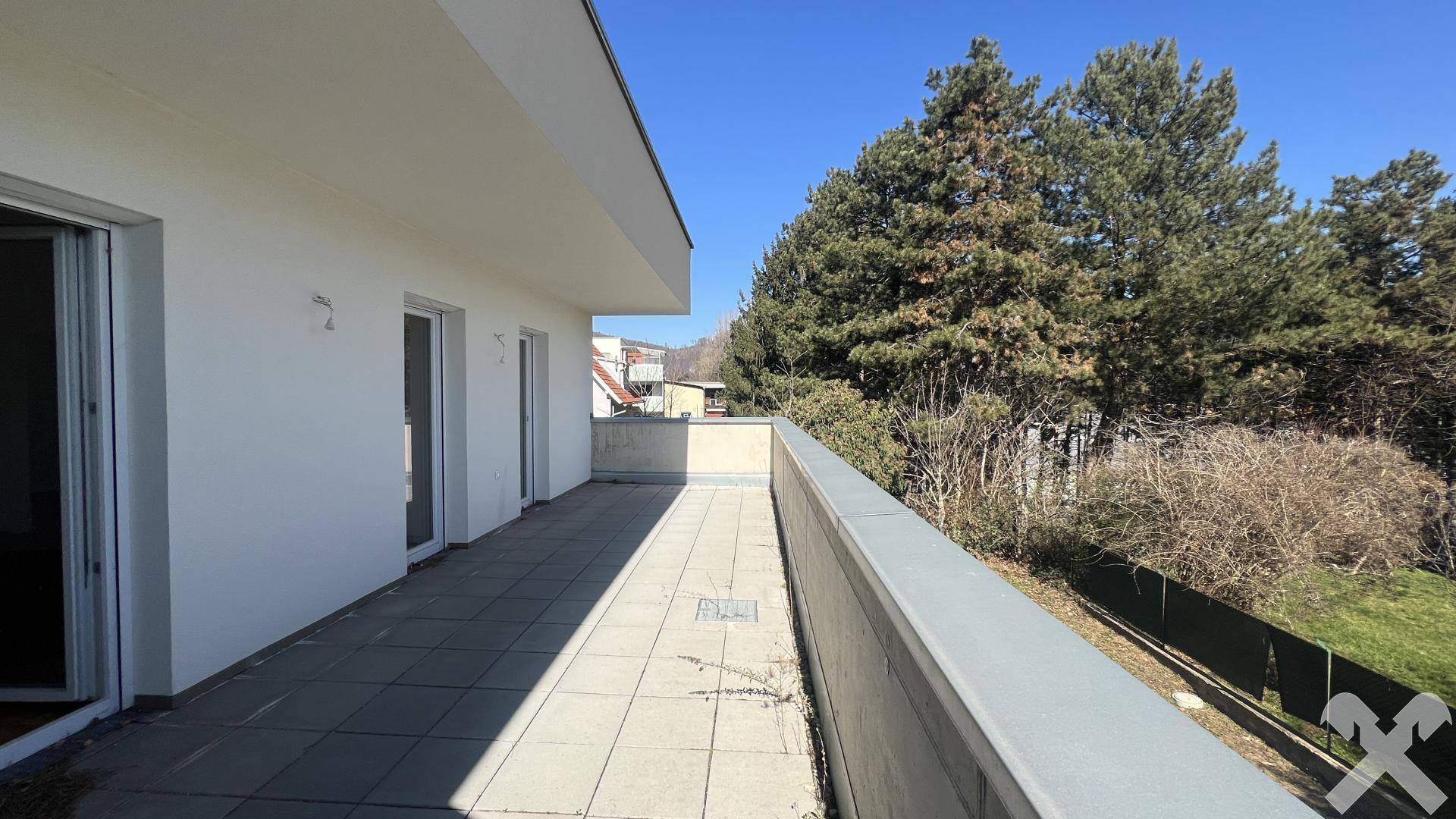 Weitläufige Terrasse mit Fliesenboden und umgebenden Bäumen unter blauem Himmel.