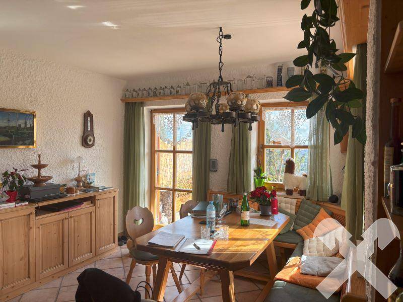 Heller Essbereich mit rustikalen Holzmöbeln, Fliesenboden und Blick ins Grüne durch die Fenster.