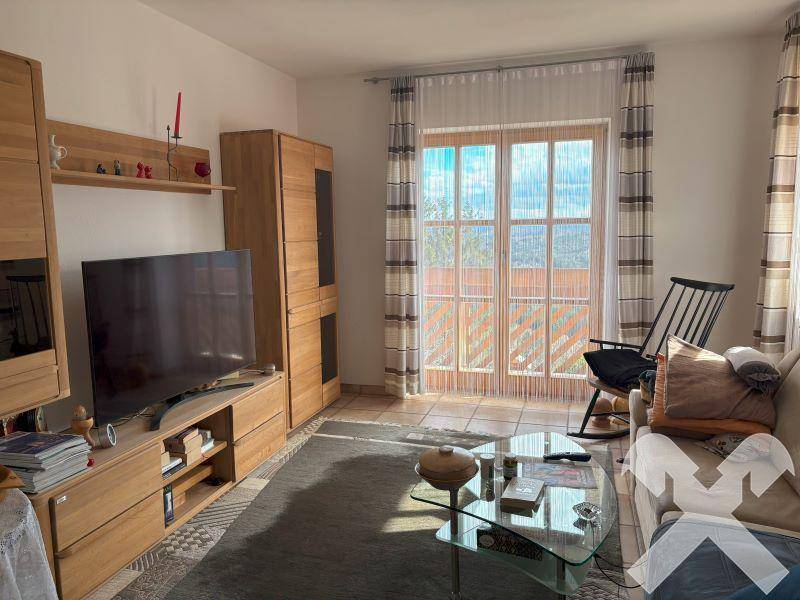 Wohnzimmer mit Holzmöbeln, Fernseher und Zugang zu einem Balkon mit weitem Ausblick.