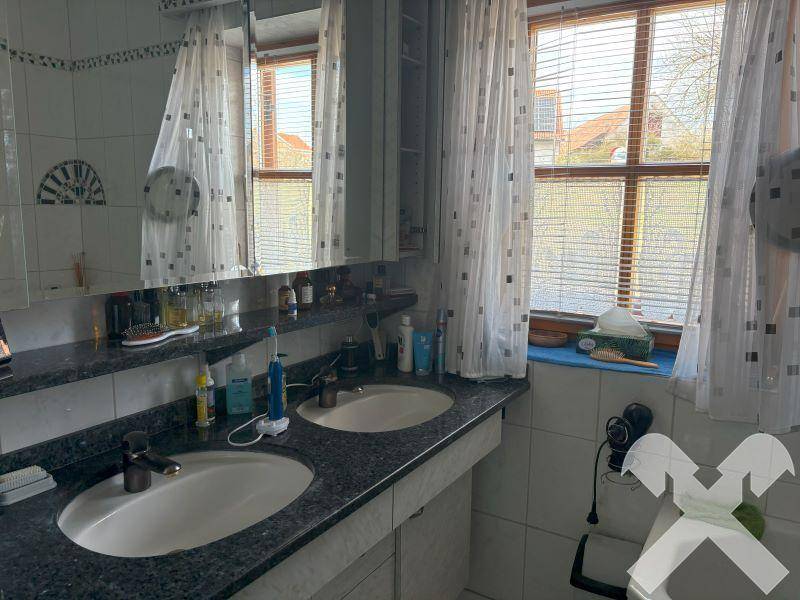 Badezimmer mit Doppelwaschbecken, großem Spiegel, Fenster und Fliesenboden.