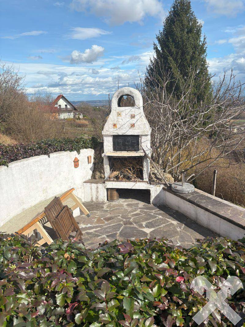 Gemütlicher Grillplatz im Freien mit Steinpflasterung und Sitzgelegenheiten, umgeben von Grün.
