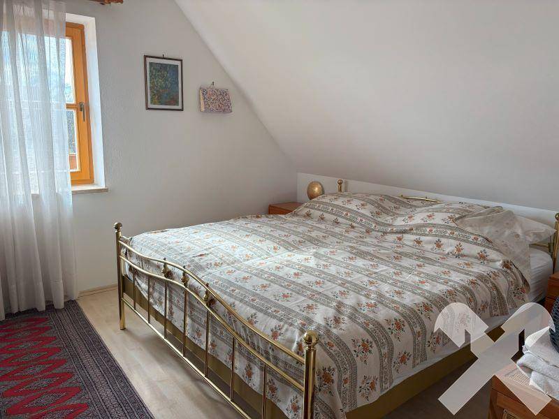Schlafzimmer im Dachgeschoss mit schräger Decke, Metallbett und Fenster.