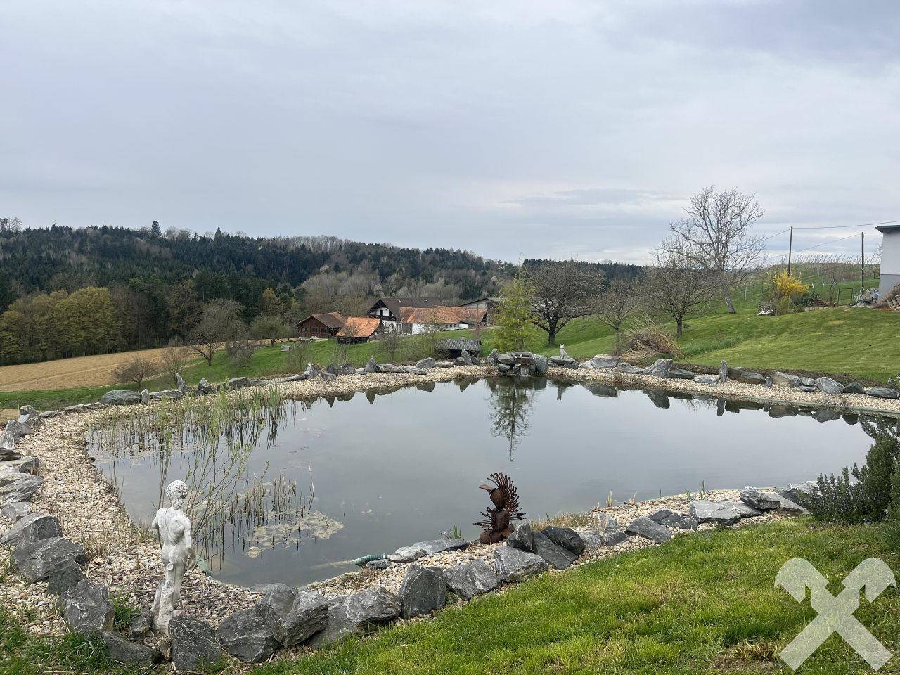 Idyllischer Gartenteich mit Steineinfassung und Blick auf die grüne Landschaft.