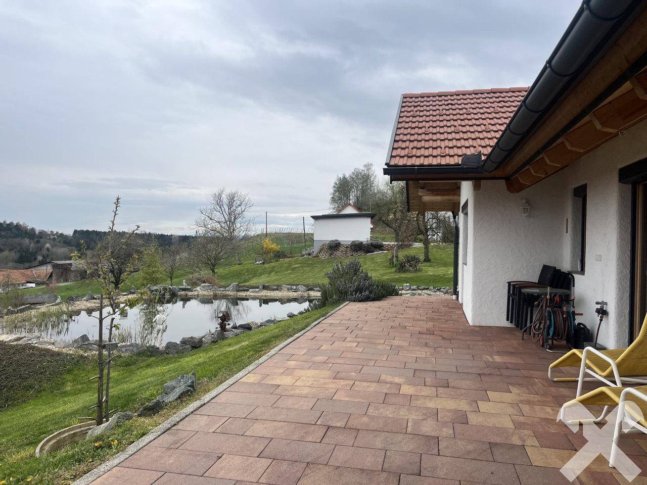 Große gepflasterte Terrasse mit Blick auf den Teich und die umliegende Natur.
