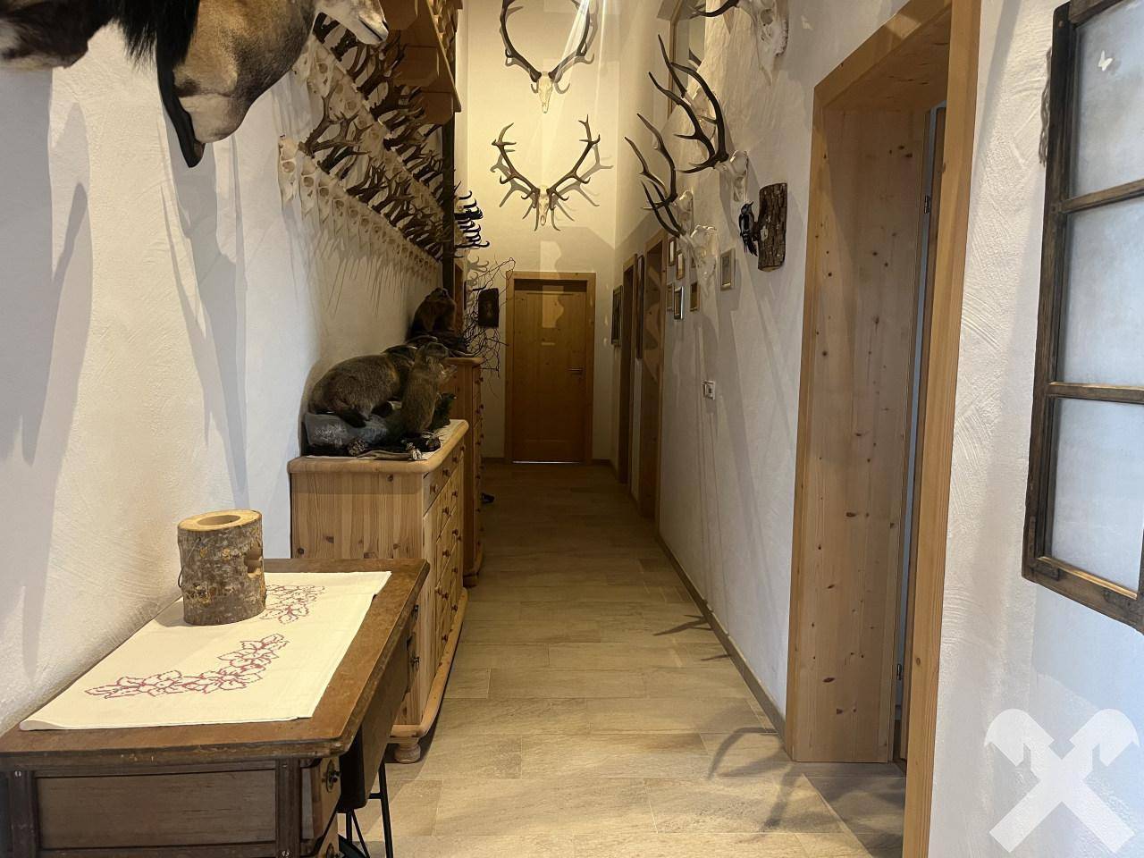 Langer Flur mit Holzbalkendecke, Fliesenboden und zahlreichen Jagdtrophäen an den Wänden.