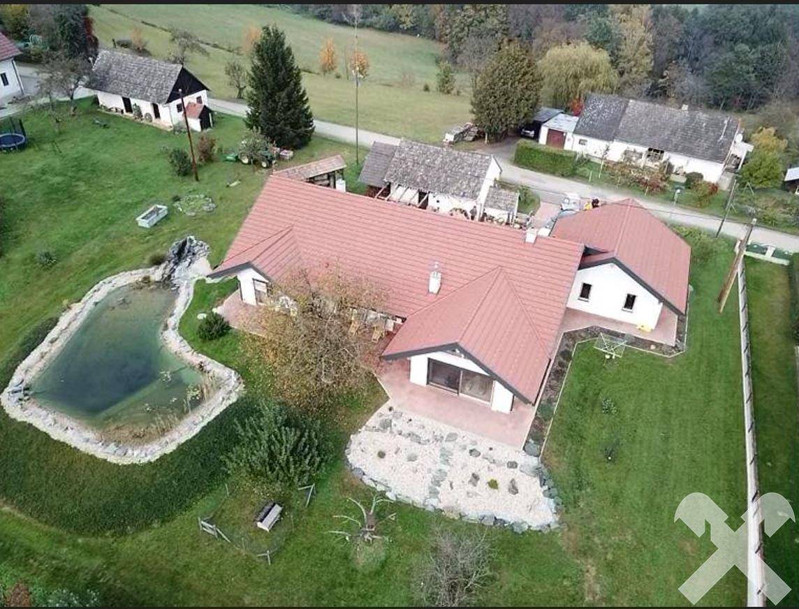 Luftaufnahme eines Hauses mit rotem Satteldach, einem Teich und weitläufiger Grünfläche in ländlicher Umgebung.