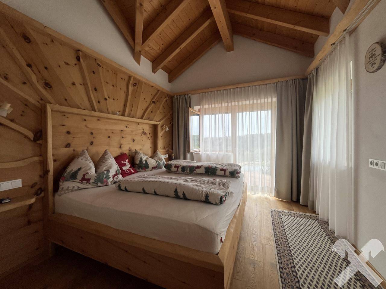 Schlafzimmer im alpinen Stil mit Holzbett, Holzwänden und Zugang zum Balkon.