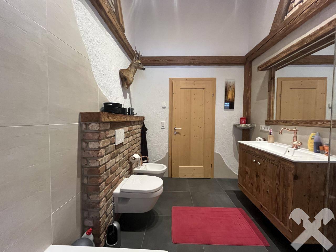 Geräumiges Badezimmer mit Holzbalken, Waschtisch aus Holz, WC, Bidet und Hirschgeweih-Dekoration.