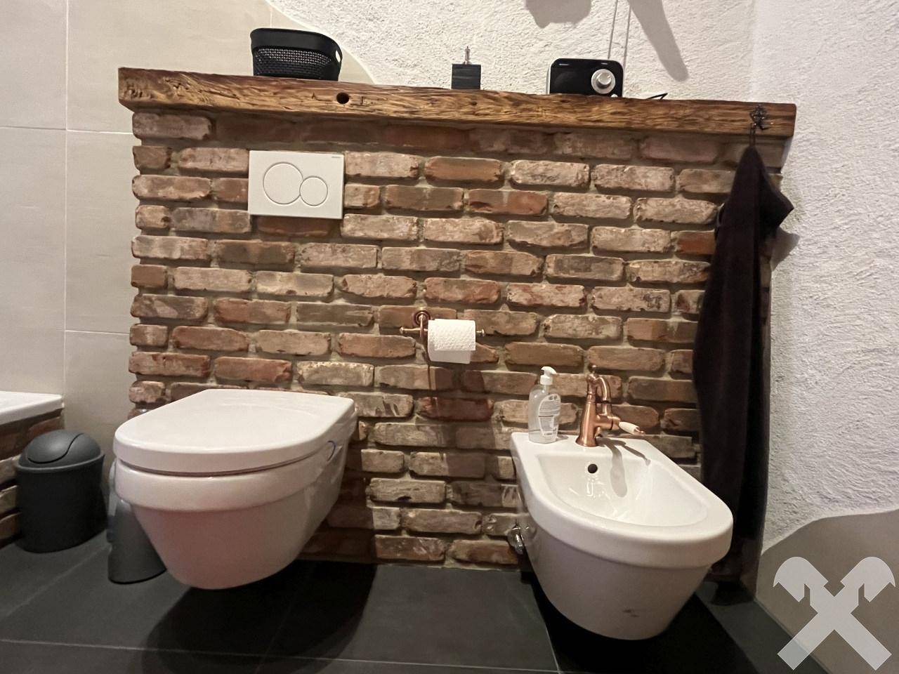 Modernes WC und Bidet mit einer rustikalen Ziegelwandverkleidung und dunklem Fliesenboden.