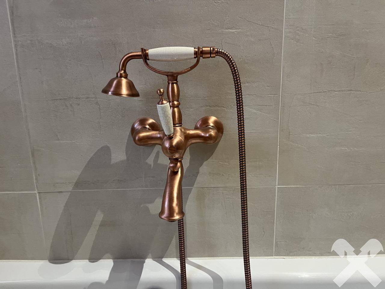 Detailaufnahme einer Badewanne mit einer eleganten Armatur in Kupferoptik und grauen Fliesen.