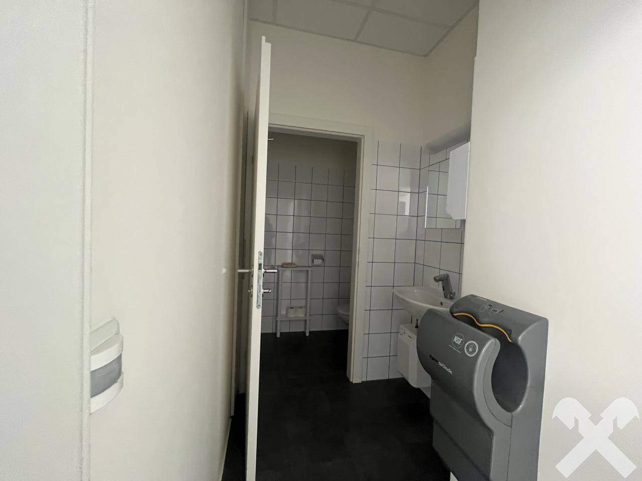 Badezimmer mit weißen Fliesen, Waschbecken und einem modernen Händetrockner, das einen sauberen Eindruck macht.