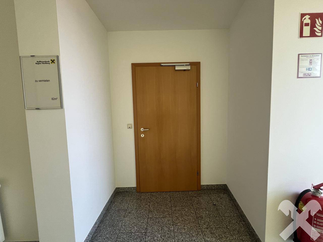 Flur mit Holztür, Granitboden und Brandschutzausrüstung, der einen sicheren Zugangsbereich darstellt.