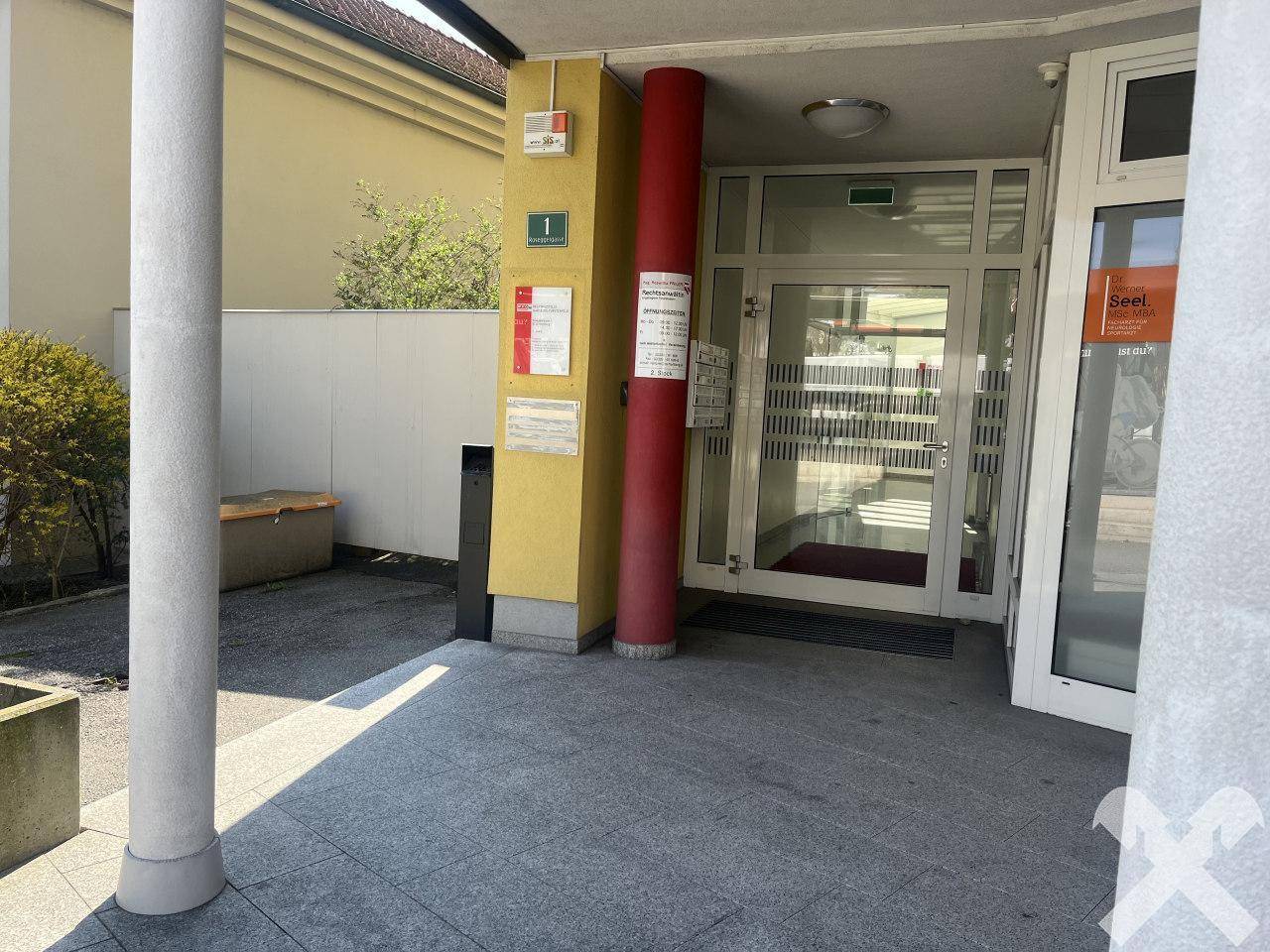 Gebäudeeingang mit Säulen, Glastüren und Beschilderung, der einen einladenden Zugang zum Gebäude bietet.
