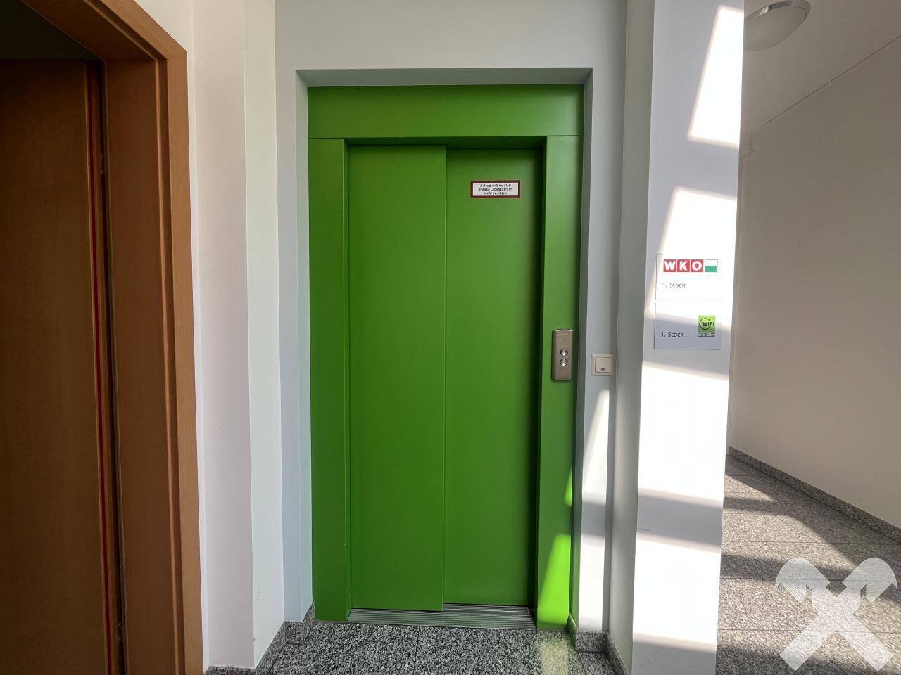 Grüner Aufzug im Flur eines Gebäudes mit Granitboden, der einen modernen und funktionalen Zugang bietet.