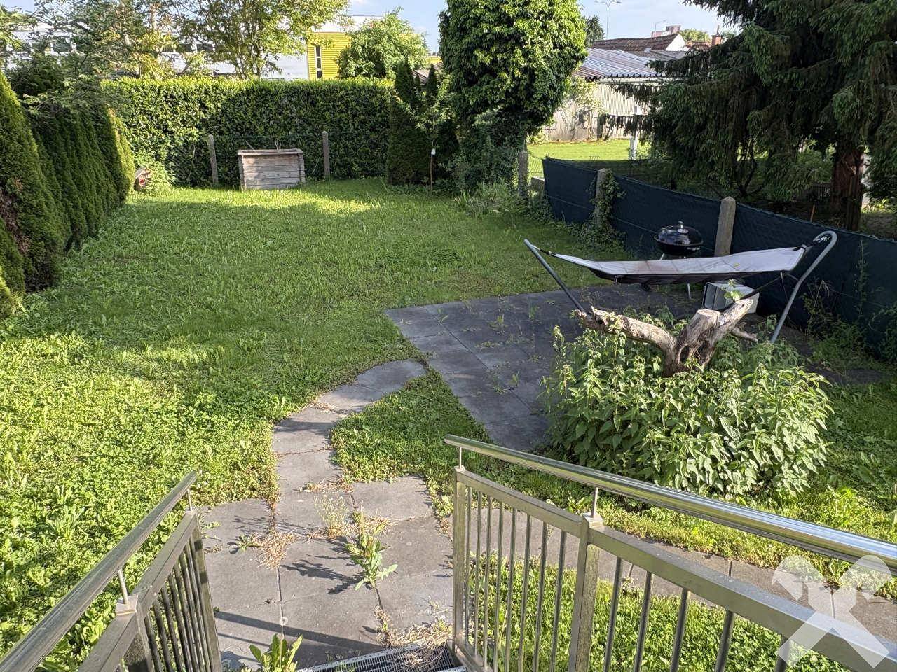 Grüner Hinterhofgarten mit Rasenfläche, gepflastertem Weg und einer Hängematte zum Entspannen.