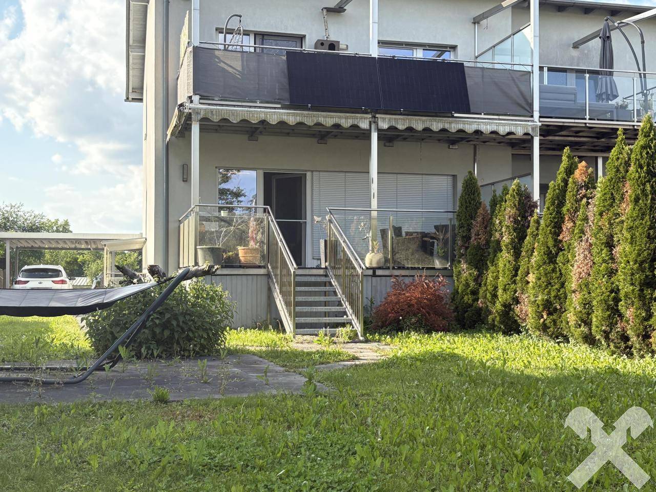 Außenansicht des Hauses mit Terrasse, Treppe zum Garten und Solarpaneelen auf dem Balkondach.