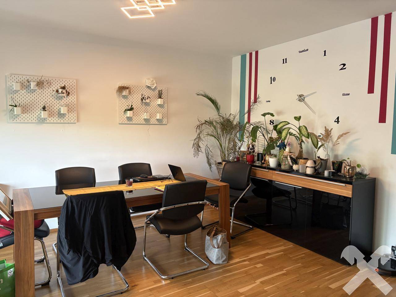 Geräumiger Essbereich mit großem Tisch, Holzfußboden und einer modernen Wanddekoration mit Uhr.