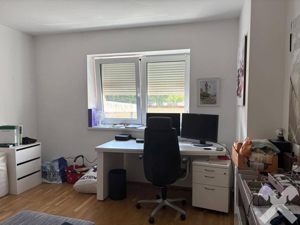 Helles Heimbüro mit Schreibtisch, Bürostuhl, zwei Monitoren und einem Fenster mit Jalousien.