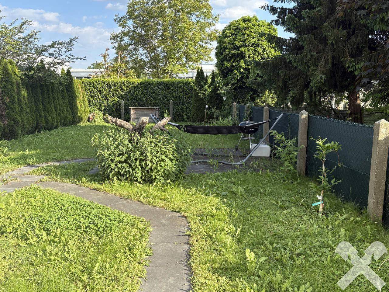 Weitläufiger Gartenbereich mit gepflegtem Rasen, hohen Hecken und einem Baum im Hintergrund.