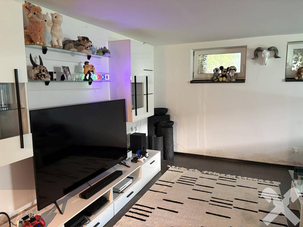 Wohnzimmer mit großem Fernseher, Unterhaltungseinheit und einem kleinen Fenster, dekoriert mit Tierköpfen.