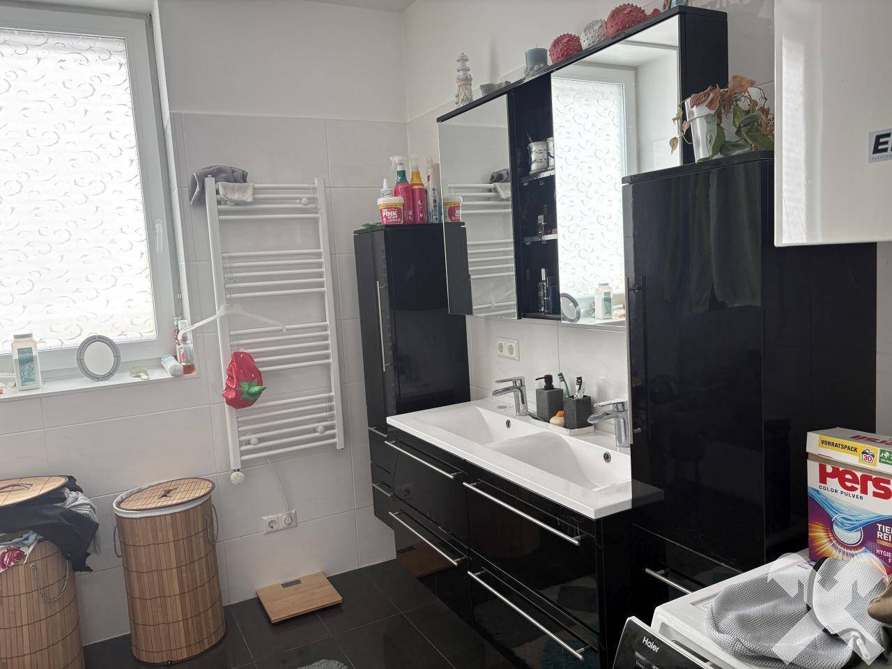 Modernes Badezimmer mit Doppelwaschbecken, Spiegelschrank, Handtuchheizkörper und einem Fenster.