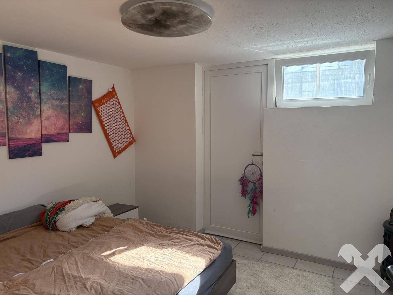 Gemütliches Schlafzimmer mit Bett, kleinerem Fenster und dekorativen Wandbildern für eine entspannte Atmosphäre.