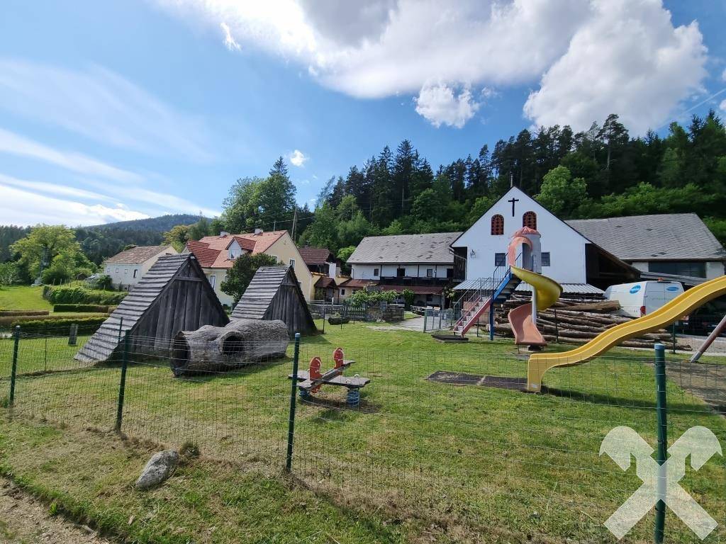 Kinderspielplatz mit Rutschen und Holzhütten vor einer Kulisse traditioneller Gebäude und Wälder.