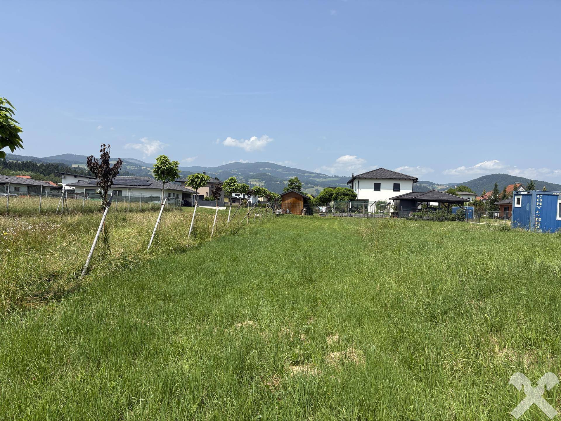 Weitläufiges Grundstück mit grüner Wiese, umgeben von Häusern und einer malerischen Berglandschaft.