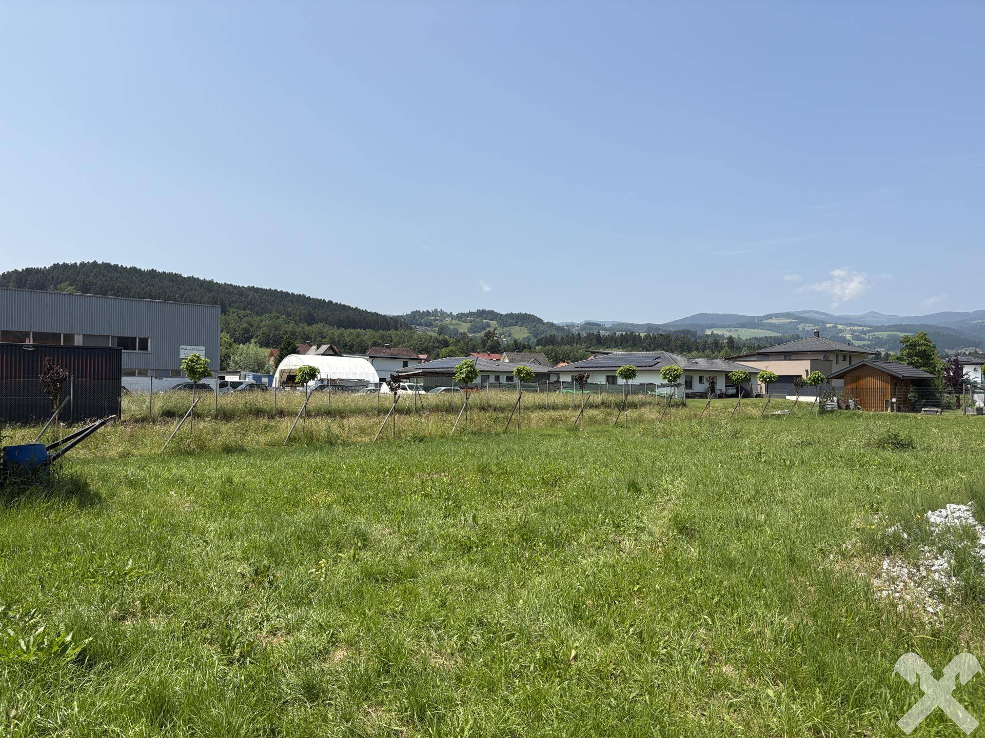 Offenes Grundstück mit Wiese, umgeben von verschiedenen Gebäuden und einer Bergkette am Horizont.