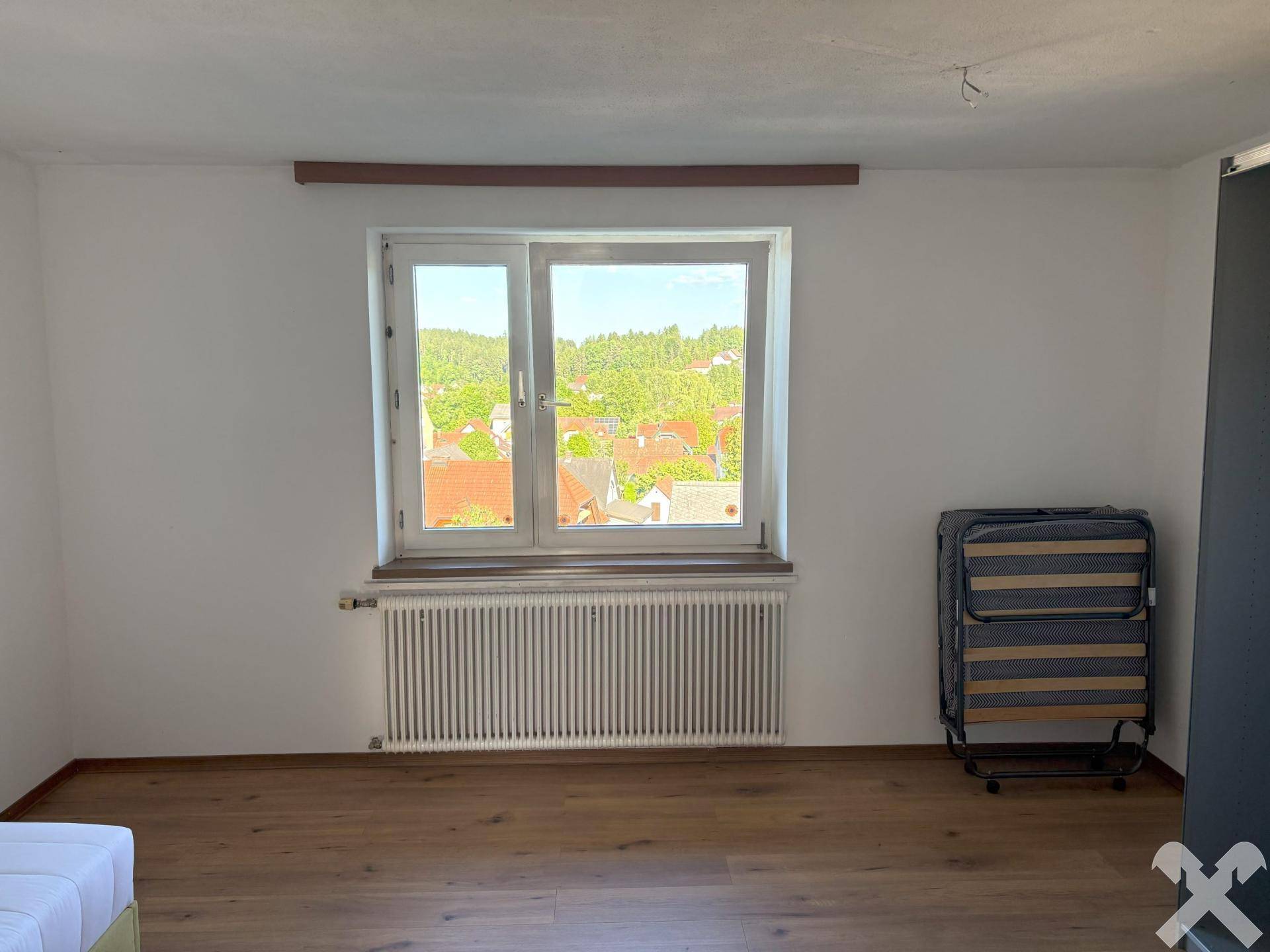 Helles Schlafzimmer mit Holzboden, großem Fenster und Blick auf die grüne Umgebung.