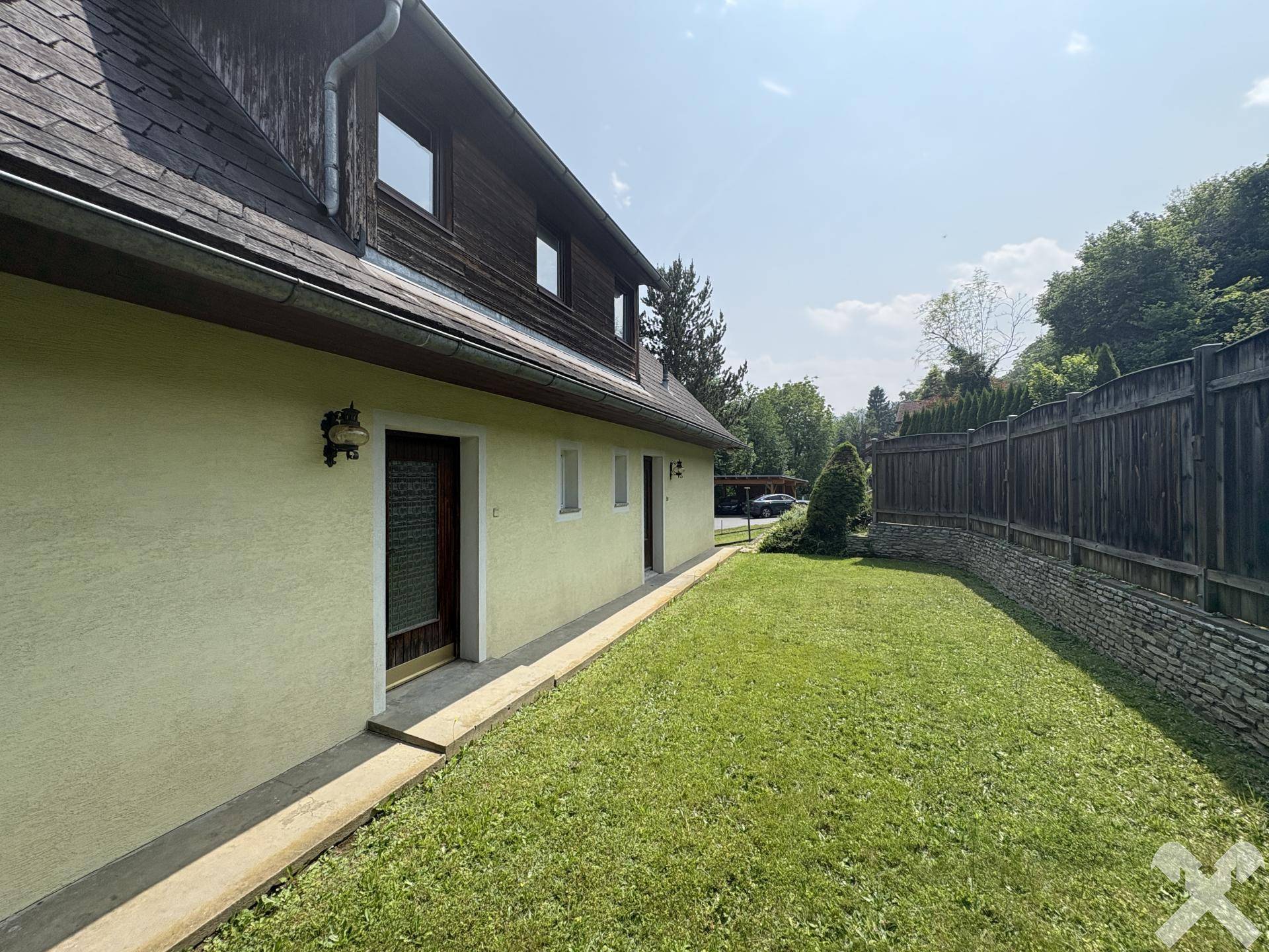 Gepflegter Rasenbereich neben dem Haus mit einer Holzwand im Hintergrund.