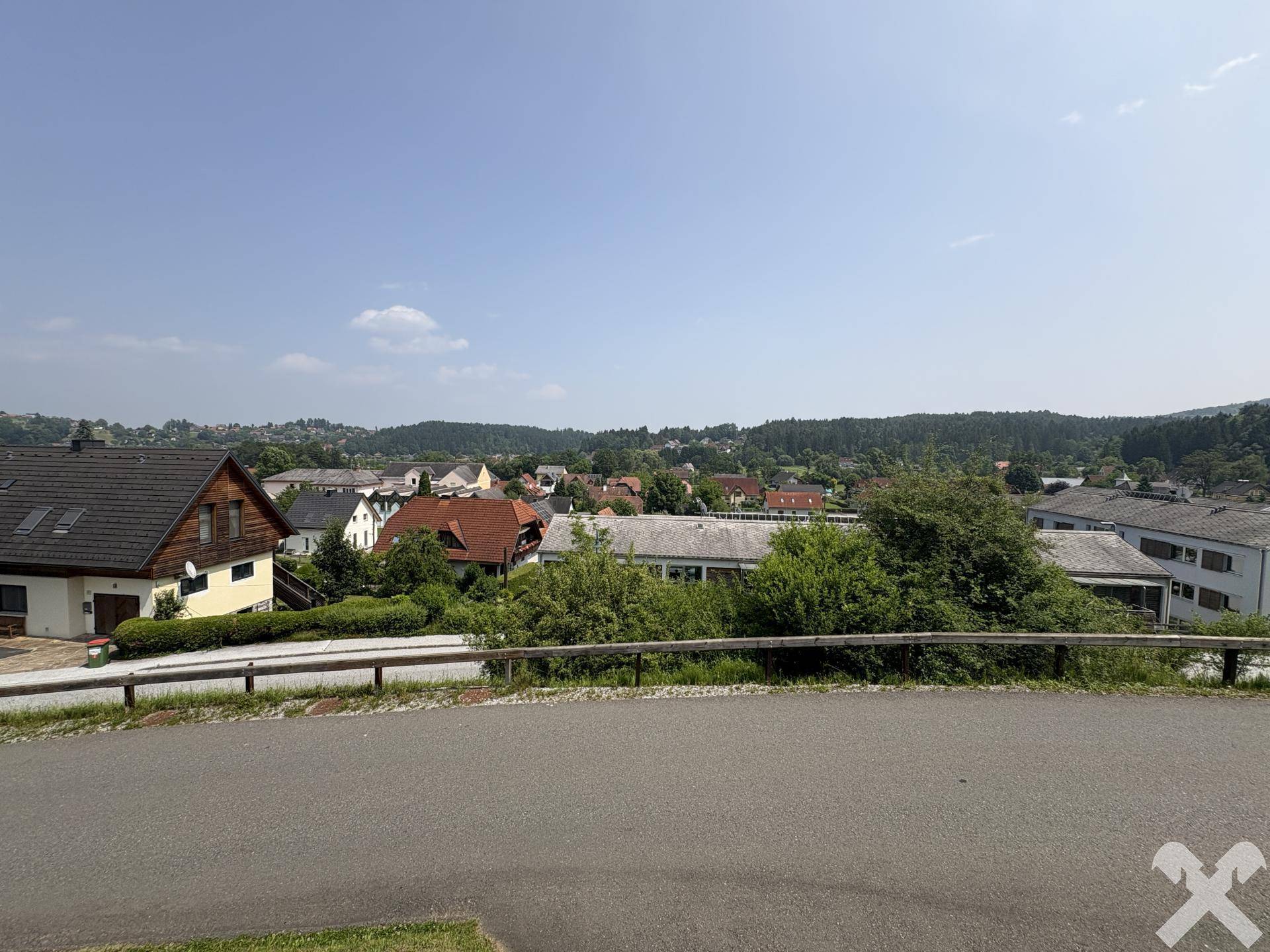 Weitläufiger Ausblick auf die ländliche Umgebung mit Häusern und bewaldeten Hügeln.