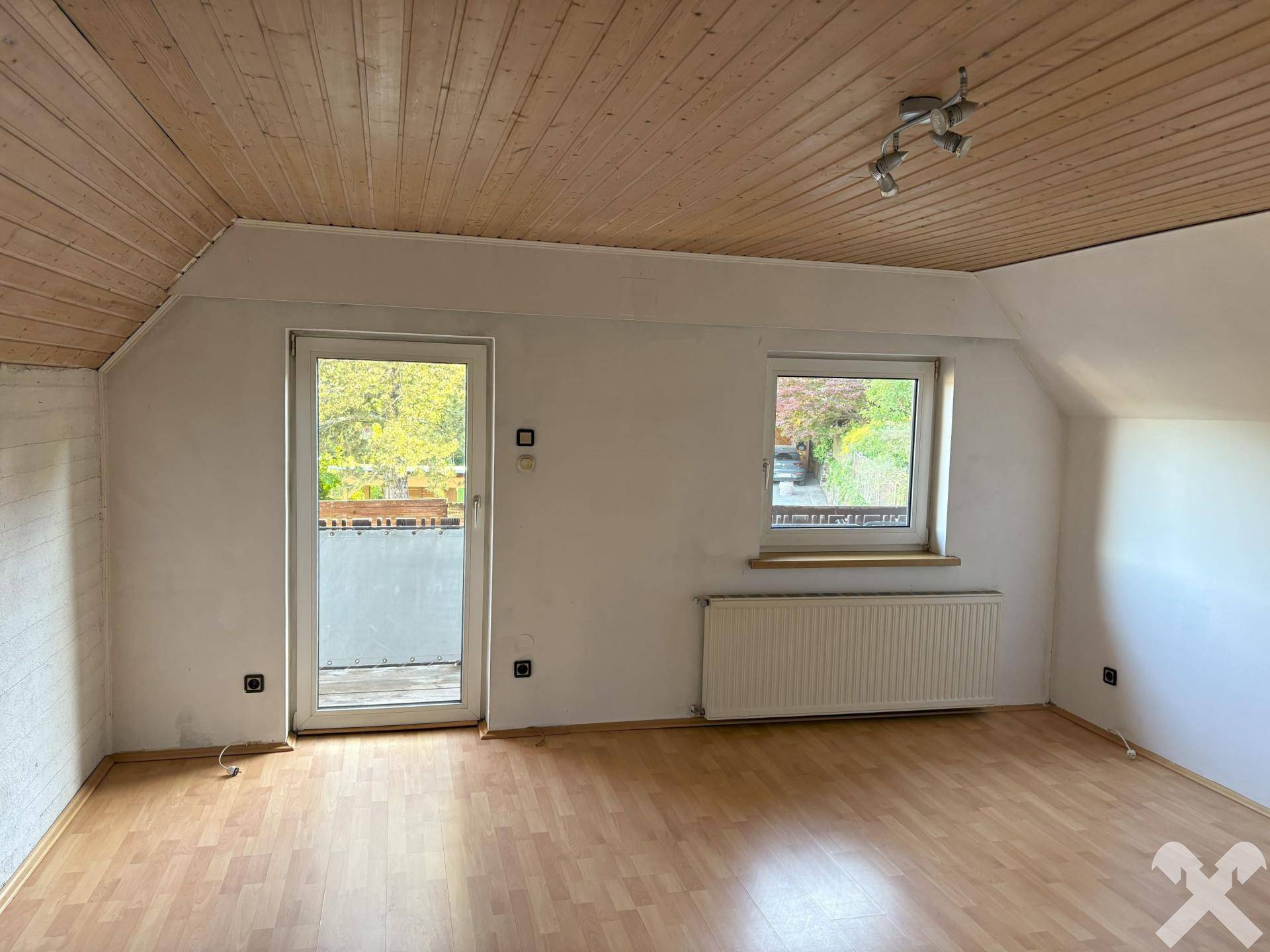 Helles Zimmer im Dachgeschoss mit Holztäfelung, Balkonzugang und Laminatboden.