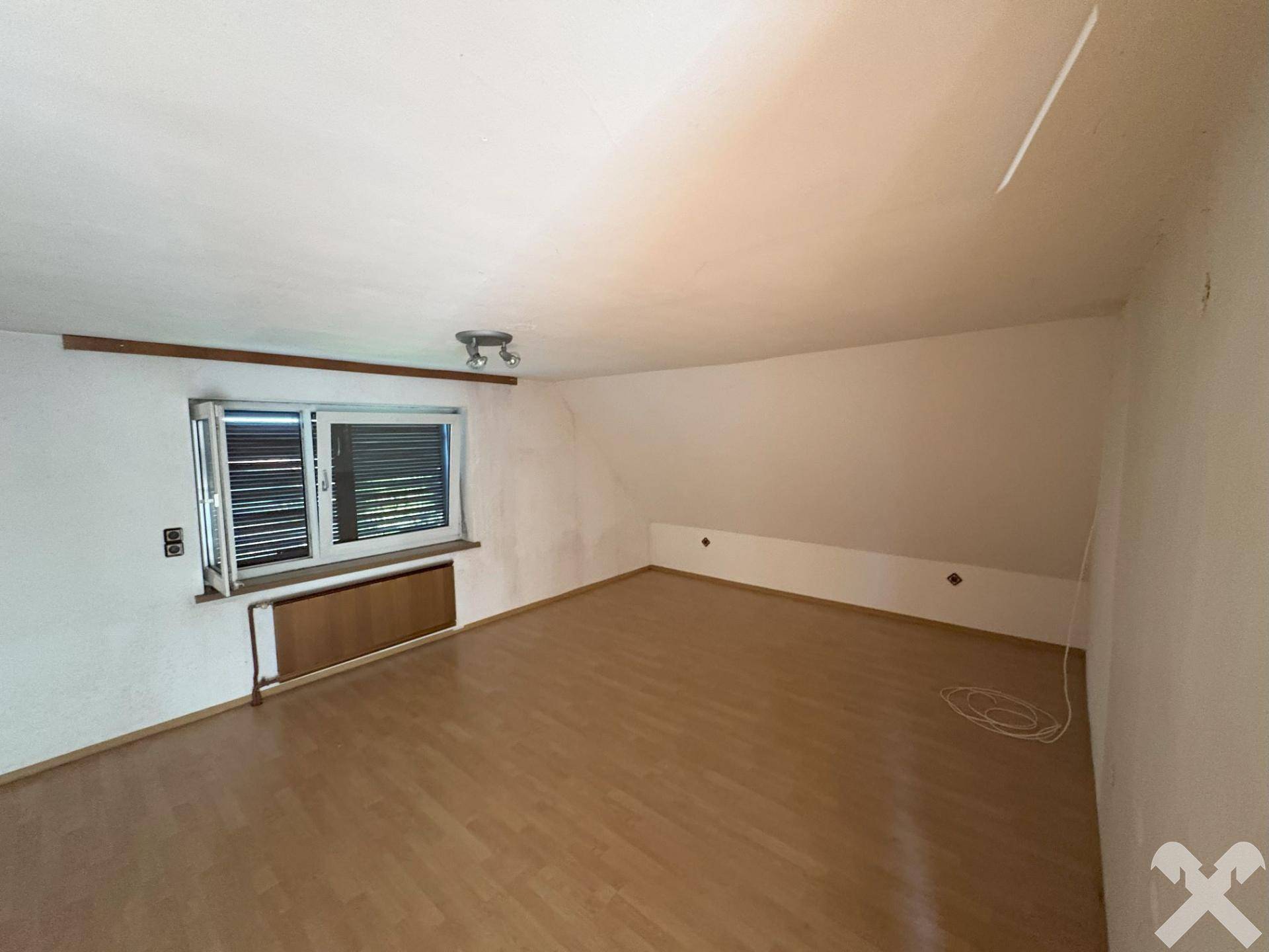 Geräumiges Zimmer im Dachgeschoss mit Laminatboden, Fenster und schräger Decke.