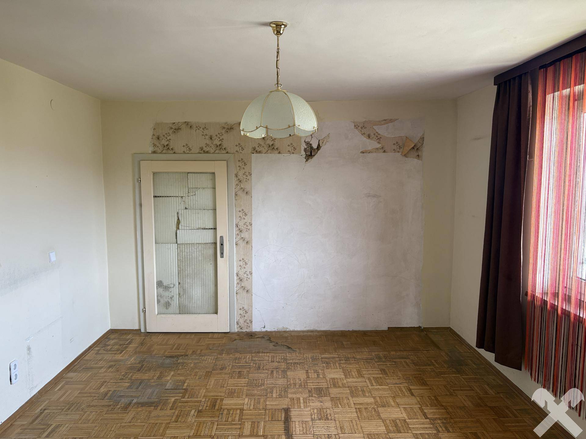 Renovierungsbedürftiges Zimmer mit Fischgrätparkett, alter Tapete und Fenster.