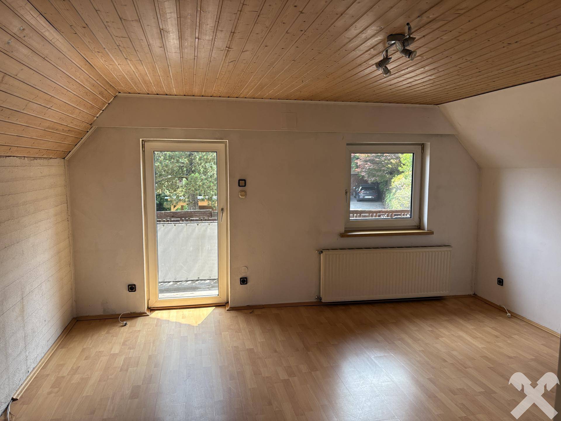 Helles Zimmer im Dachgeschoss mit Holztäfelung, Balkonzugang und Laminatboden.