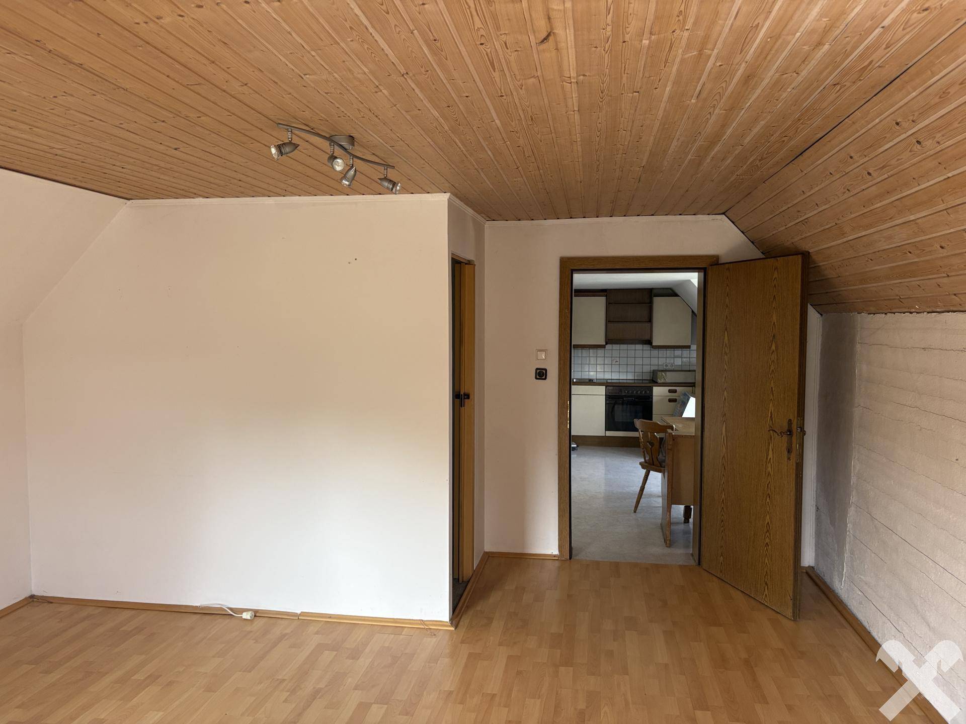 Geräumiges Zimmer im Dachgeschoss mit Holztäfelung und Zugang zu einem weiteren Raum.