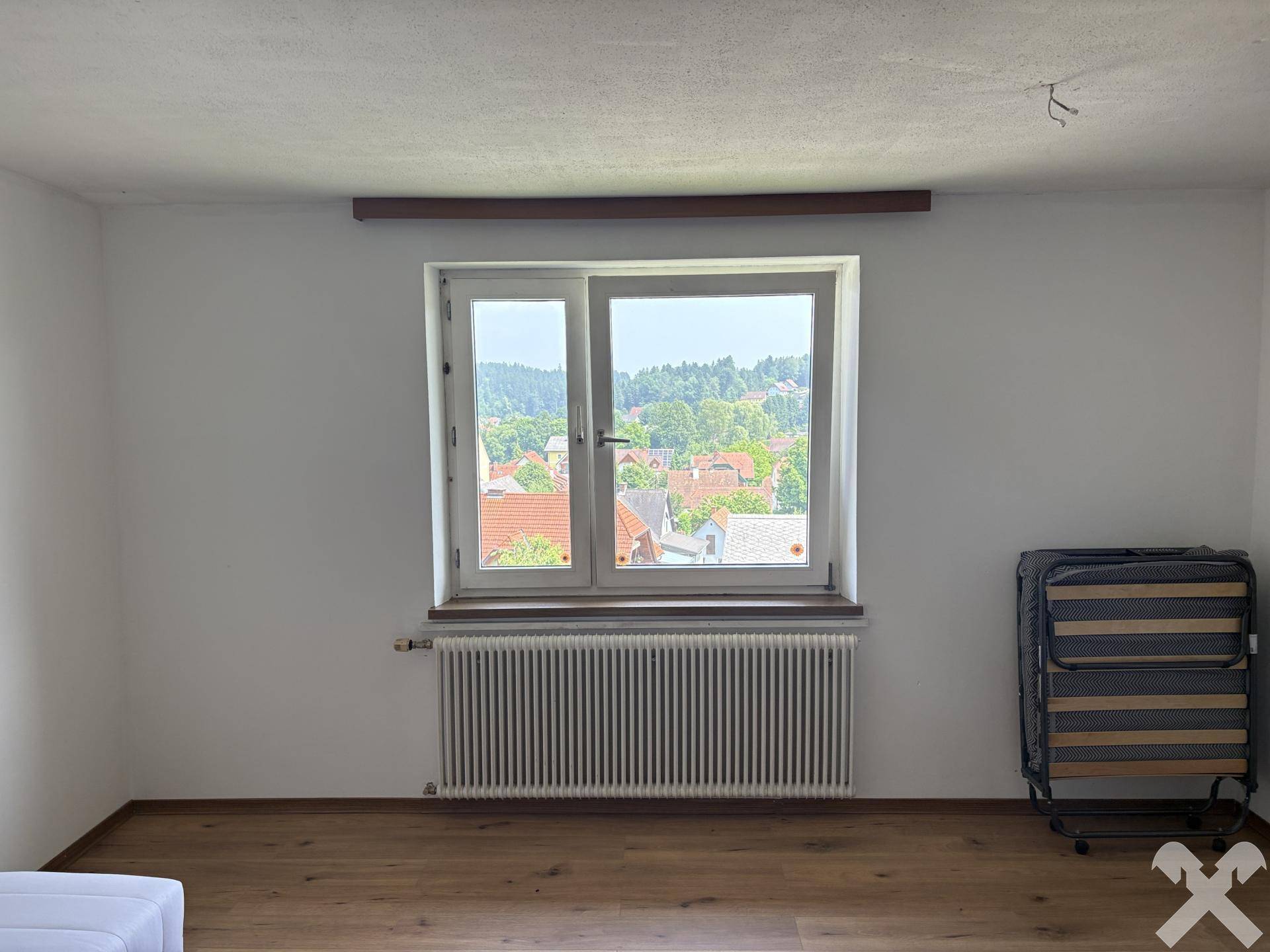Helles Schlafzimmer mit Holzboden, großem Fenster und Blick auf die grüne Umgebung.