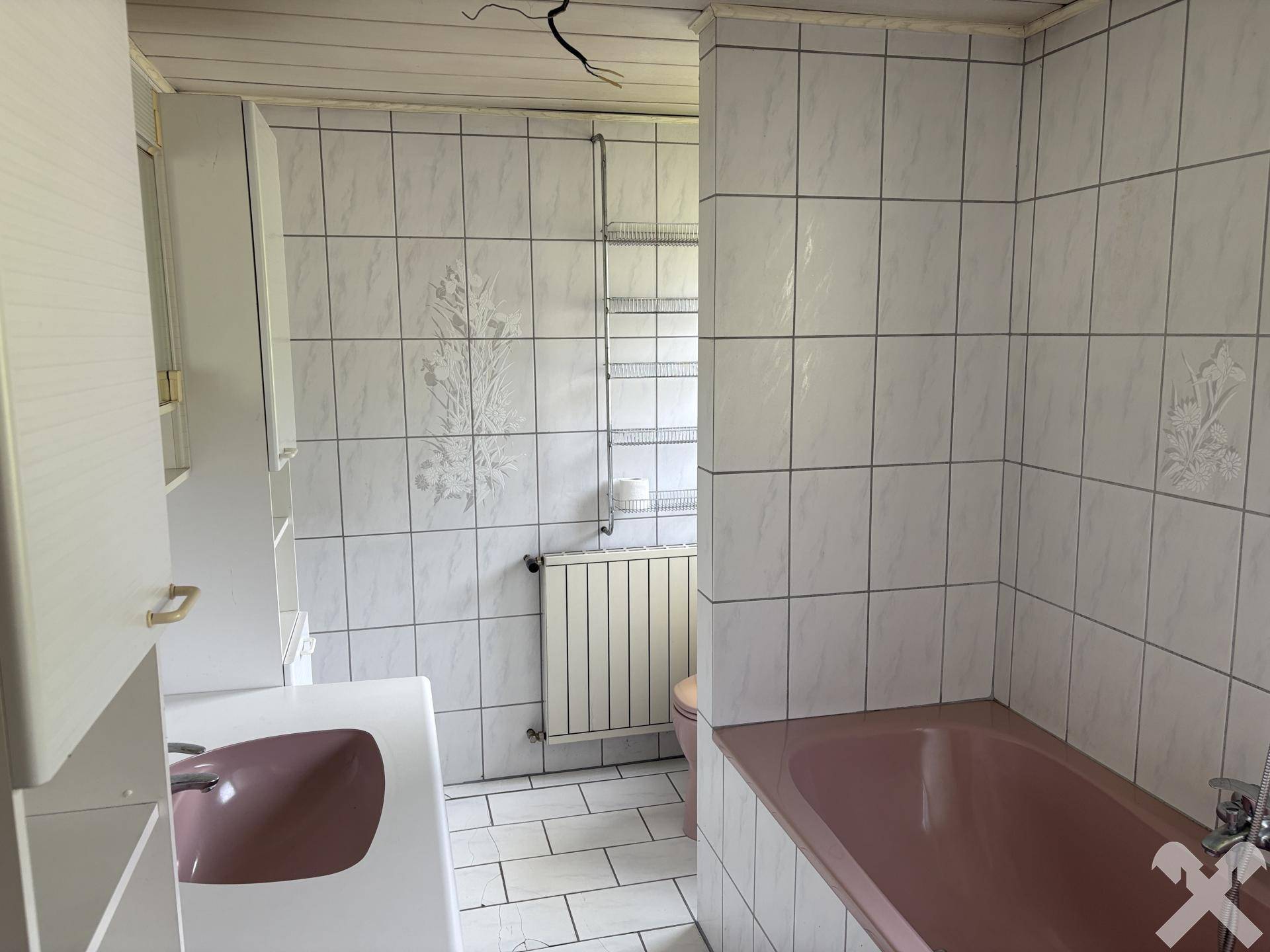 Badezimmer mit rosa Badewanne, Waschbecken und weißen Fliesen im Retro-Stil.